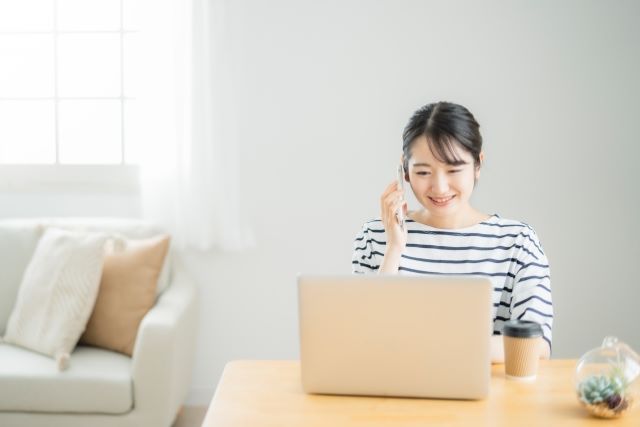 パソコンを見ながら電話する女性